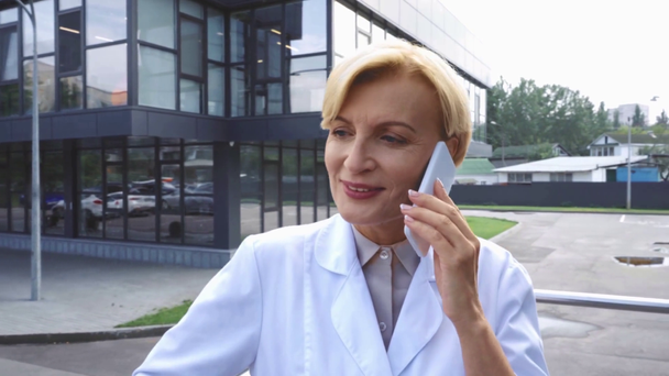 arts van middelbare leeftijd praten op smartphone in de buurt van kliniek  - Video