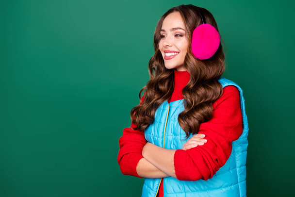 Profile photo of cute lovely young lady folded hands self-assured cheerful look empty space waiting friend wear pink ear warmers blue vest red sweater isolated green color background - Фото, зображення