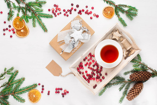 自然のクリスマスの装飾、お茶のカップ、クリスマスの贈り物、クランベリー、白い木製の背景に松のコーンと枝。フラットレイアウト、トップビュー。休日テキストのための空のスペース. - 写真・画像