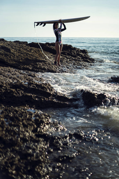 A vertical shot of a female carrying a surfboard to the ocean - Foto, afbeelding