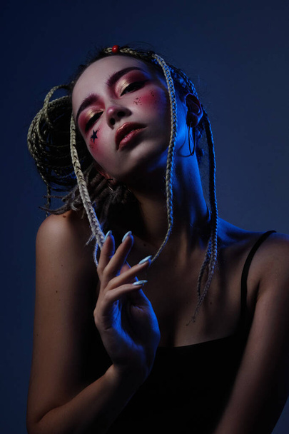 girl with dreadlocks in a black top with creative makeup posing in the studio with blue light - Foto, immagini
