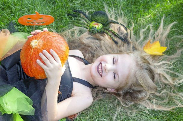 girl in a witch costume for the Halloween holiday. Happy girl lies on the grass - Foto, imagen
