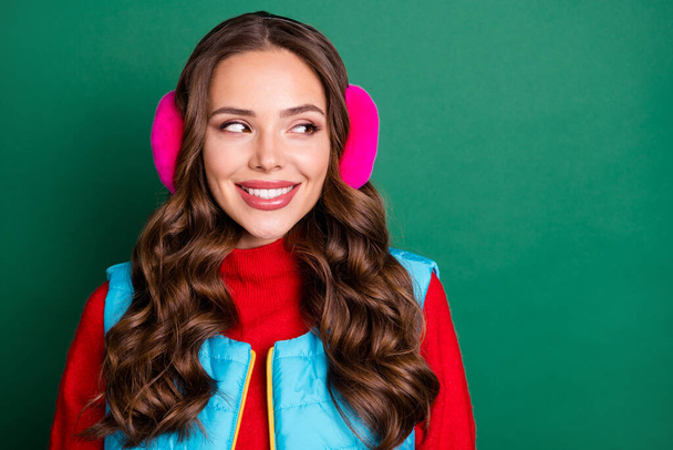 Close up photo of charming pretty young lady beaming smiling interested look side empty space watch snowfall wear pink ear warmers blue vest red pullover isolated green color background - Photo, image