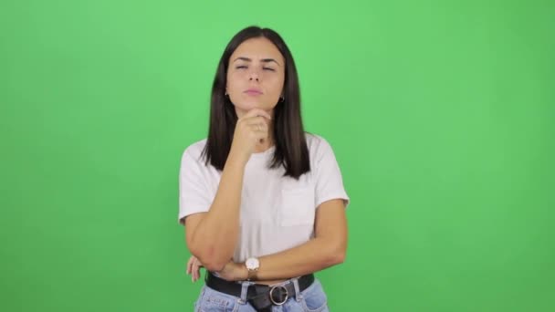 Fiatal gyönyörű nő elszigetelt zöld háttér néz oldalra, és gondolkodás az ujjával az állában - Felvétel, videó