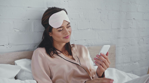 Lächelnde Frau plaudert auf Smartphone im Bett - Filmmaterial, Video