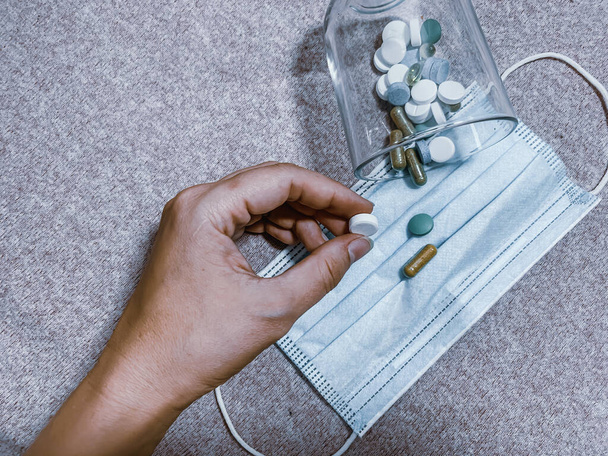 A hand holding a pill, pills on a face mask - Valokuva, kuva