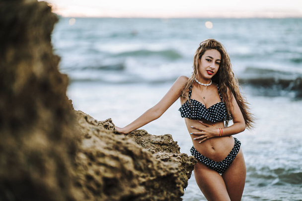 A sexy caucasian woman wearing a spotted swimsuit and posing on a beach - Foto, afbeelding