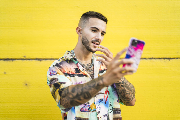 A young Caucasian man with tattoos taking selfies on a yellow background - Foto, afbeelding