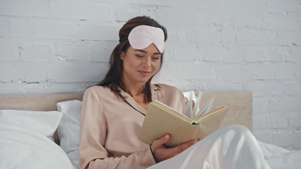 uśmiechnięta kobieta czyta książkę w łóżku - Materiał filmowy, wideo