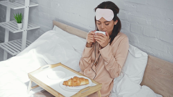 young woman drinking coffee in bed and smiling at camera - Felvétel, videó