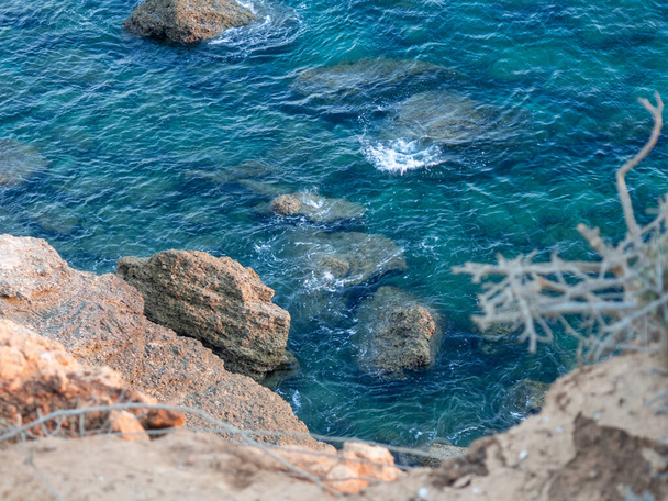 A high angle shot of the clear blue water near the rocky shore during daylight - Foto, Imagem