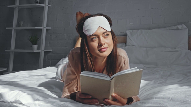 descalza mujer leyendo libro y mirando hacia otro lado en la cama - Metraje, vídeo