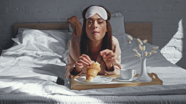morena mujer viendo tv mientras desayuna en la cama - Metraje, vídeo