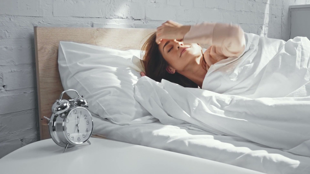 brunette nainen kääntämällä herätyskello ja venyttely sängyssä - Materiaali, video
