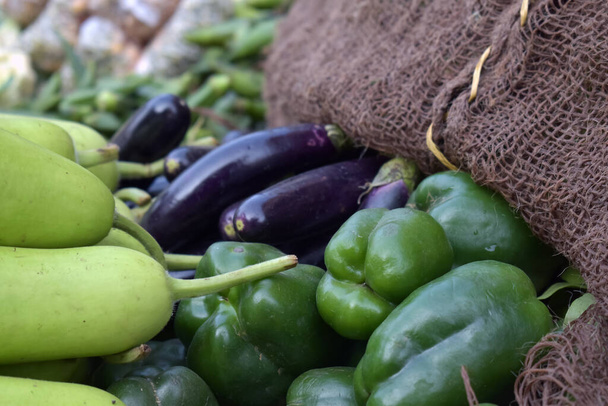 A closeup shot of eggplants, green bell peppers, and bottle gourd in a market place - Фото, изображение
