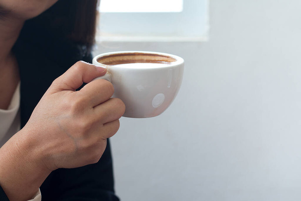 Una mujer de negocios sostiene una taza de café blanco durante el trabajo en la oficina. - Foto, imagen