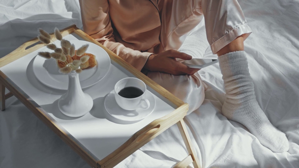 vista cortada da mulher conversando no smartphone perto do café da manhã n cama - Filmagem, Vídeo