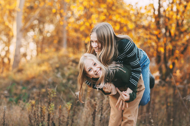 Twee gelukkige kleine meisjes zusjes lachen, plezier hebben en spelen in de herfst in de natuur buiten in het herfstpark - Foto, afbeelding