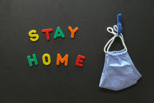 The colorful letters "Stay Home" and a mask on a black surface - Foto, afbeelding