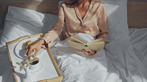 vista recortada de la mujer desayunando y leyendo en la cama - Metraje, vídeo