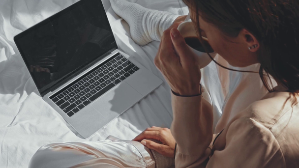 vista aerea di freelance bere caffè e digitando sul computer portatile a letto - Filmati, video
