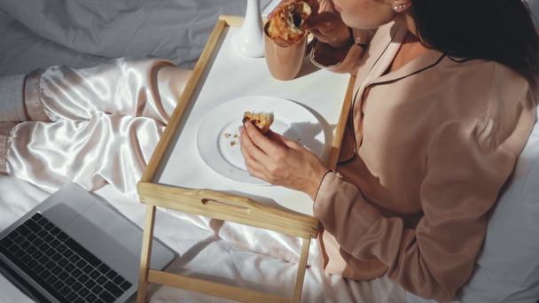 wolny strzelec jedzący rogaliki i pijący herbatę w łóżku - Materiał filmowy, wideo