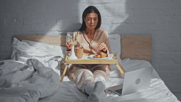 χαρούμενος ελεύθερος επαγγελματίας λαμβάνοντας πρωινό κοντά στο φορητό υπολογιστή στο κρεβάτι - Πλάνα, βίντεο