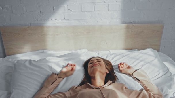 mujer despierta cayendo sobre almohadas con las manos extendidas - Imágenes, Vídeo