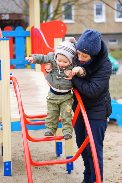 POZNAN, POLAND - Jan 08, 2015: Woman helping toddler on a equipment at a playground on a cold day - Foto, immagini