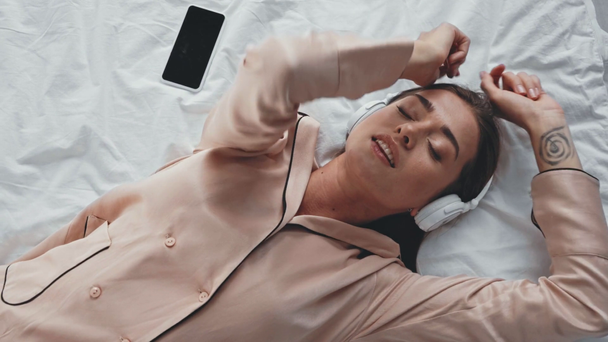 Ευτυχισμένη γυναίκα ακούγοντας μουσική στα ακουστικά, ενώ βρίσκεται στο κρεβάτι - Πλάνα, βίντεο