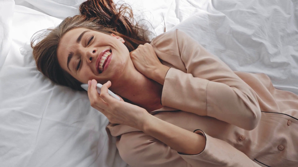 Yatakta yatarken cep telefonuyla konuşan mutlu bir kadının üst görüntüsü. - Video, Çekim