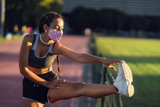 A beautiful female exercising with a protective face mask in the park- COVID-19 - Foto, imagen