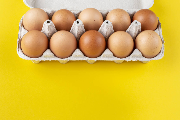 Chicken eggs in an open egg carton isolated on yellow. Top view with copy space. Natural healthy food and organic farming concept.  - Foto, Imagen