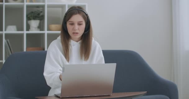 若い女性は、自宅で働く、オンライン教師の勉強とノートパソコンの話を呼び出すヘッドセット会議を身に着けています。コンピュータのウェブカメラのチャットを使用して学ぶ女性学生はノートを作る。距離教育の概念 - 映像、動画