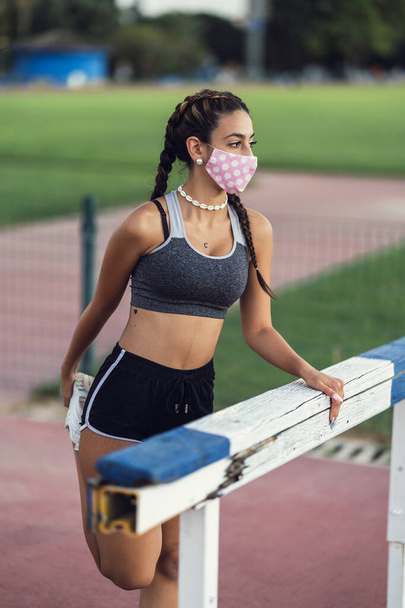 A shallow focus of a young female with a facemask in sportswear stretching in a park - Zdjęcie, obraz