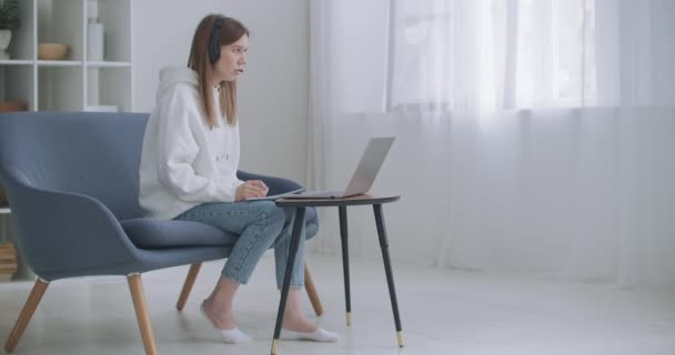 Genç bir kadın kulaklık takıyor. İnternette öğretmeniyle bilgisayar başında konuşuyor. Evde çalışıyor. Bilgisayar kamerası kullanarak öğrenen bayan öğrenci notlar alır. Uzaklık eğitimi kavramı - Video, Çekim