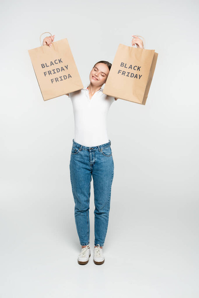 young woman with closed eyes holding shopping bags with black friday lettering on white - Photo, Image