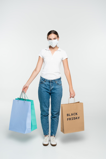 Nuori nainen lääketieteellinen naamio tilalla ostoskassit musta perjantai kirjoitus valkoinen  - Valokuva, kuva