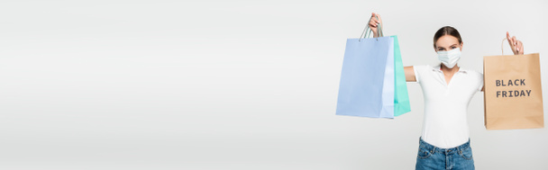cultivo panorámico de mujer joven en máscara médica sosteniendo bolsas de compras con letras de viernes negro en blanco  - Foto, Imagen