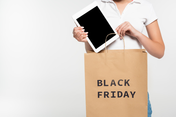 cropped view of woman putting digital tablet with blank screen in shopping bag with black friday lettering isolated on white  - Photo, Image