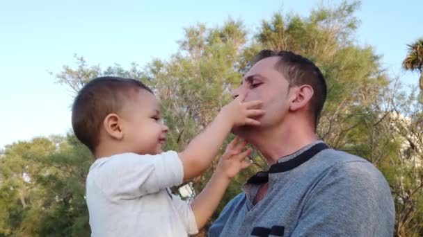 Genç beyaz bir baba oğlunu kucağında tutuyor. Bebek babasının yüzüne dokunuyor ve ikisi de komik suratlar yapıyor. - Video, Çekim