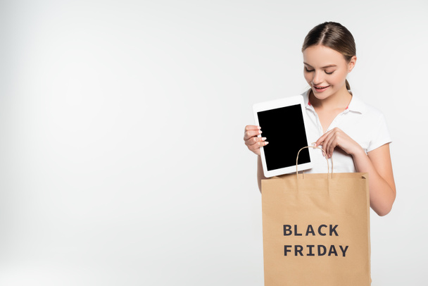 Genç bir kadın dijital tableti işaret ediyor. Beyaz harflerle izole edilmiş siyah cuma harfleriyle alışveriş çantasının yanında boş bir ekran var.  - Fotoğraf, Görsel