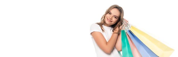 panoramic concept of pleased young woman holding colorful shopping bags and looking at camera isolated on white - Photo, Image