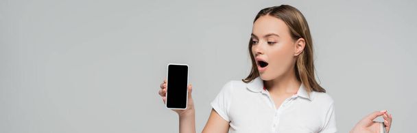 панорамна концепція шокованої жінки, дивлячись на смартфон з порожнім екраном ізольовано на сірому
  - Фото, зображення