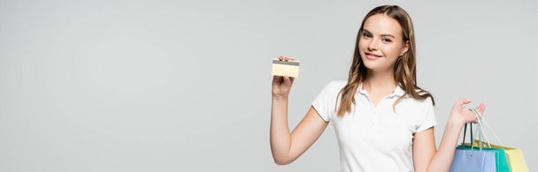 concepto panorámico de mujer joven complacida sosteniendo tarjetas de crédito y bolsas de compras aisladas en gris, concepto de viernes negro - Foto, Imagen