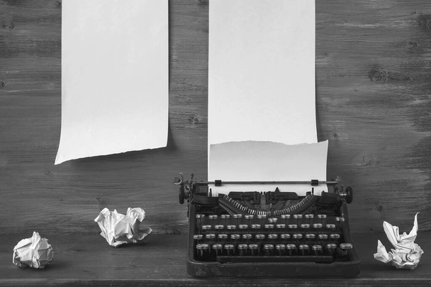 Vanha musta kirjoituskone paperilla ja rypistynyt paperiarkkeja sijoitettu pöydälle.Musta ja valkoinen kuva - Valokuva, kuva