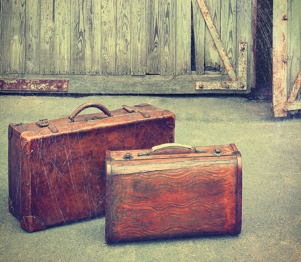 Two old travel leather suitcases stand against the background of open garage doors. Stylized photo - Photo, Image