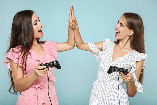 Young happy girlfriends playing computer game with joysticks on blue background - Foto, afbeelding