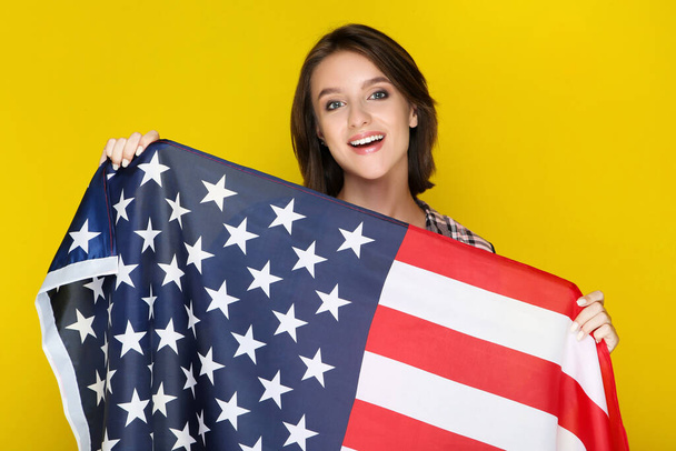 Hermosa joven sosteniendo bandera americana sobre fondo amarillo - Foto, imagen