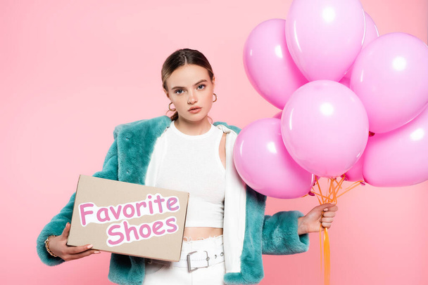 young woman holding carton box with favorite shoes lettering and balloons on pink  - Photo, Image